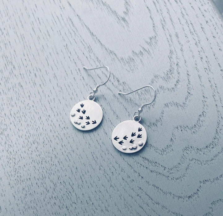 Two round silver earrings with bird footprint designs