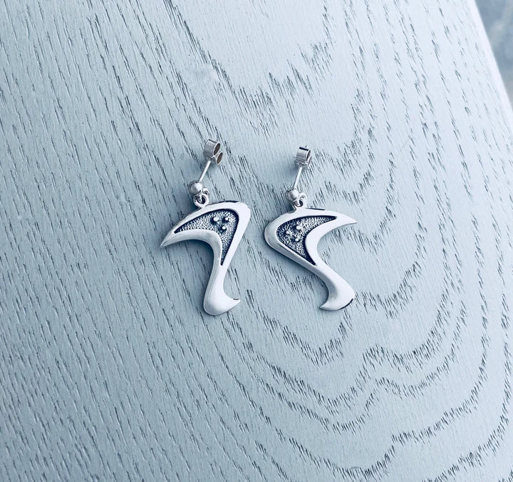 Silver highheeled shoe earrings with black accents on textured wood