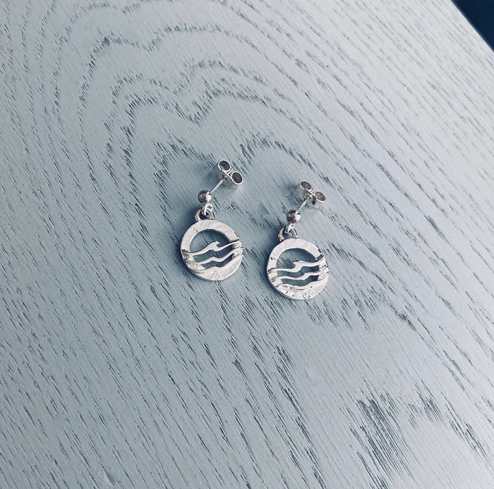 Silver earrings with circular wave designs on a textured light blue wooden surface