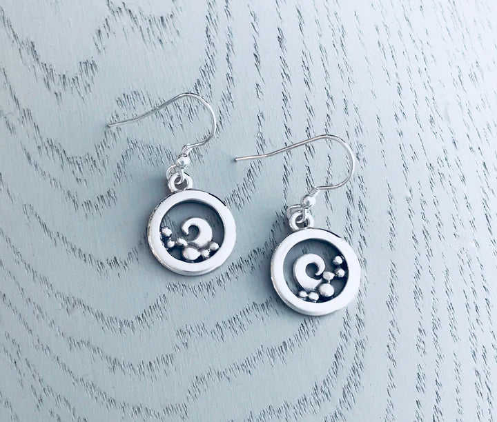 Silver round earrings with swirl design on a grey wooden base